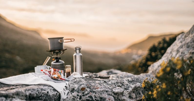 Outdoor Cooking - Cooking Pot on a Portable Stove Beside a Steel Tumbler