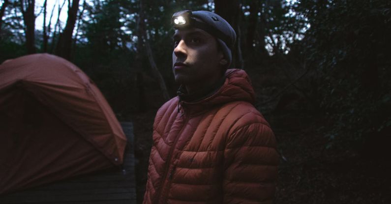 Camping Gear - Man in a Winter Jacket and a Headlamp next to a Tent in the Forest