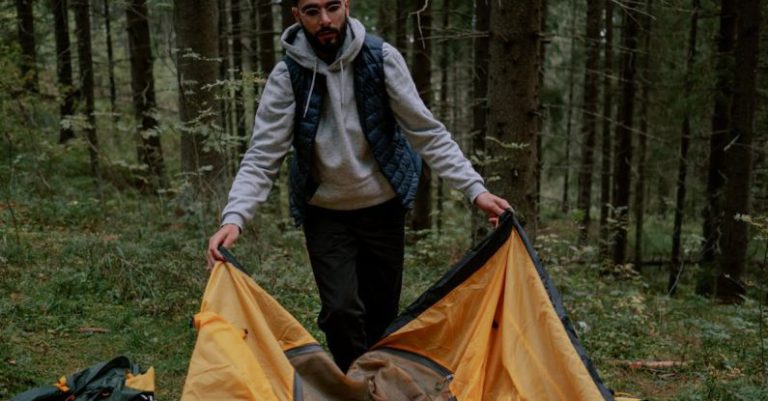 Camping Gear - Man in Blue Gilet Setting Up a Tent